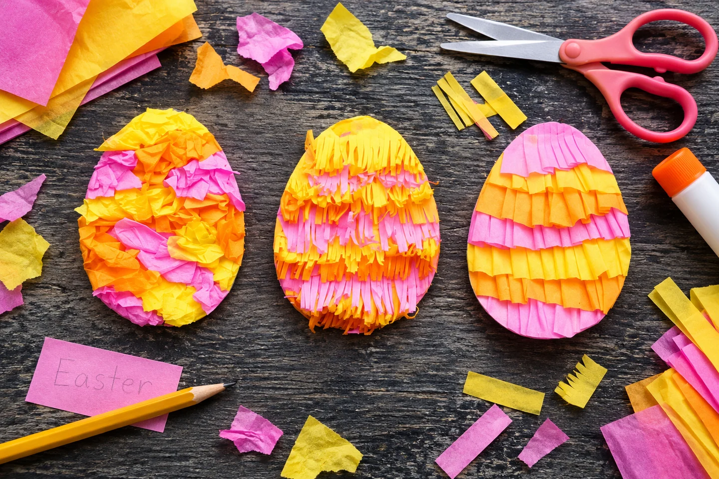 Three flat Easter egg crafts made with pink and yellow paper on a dark table