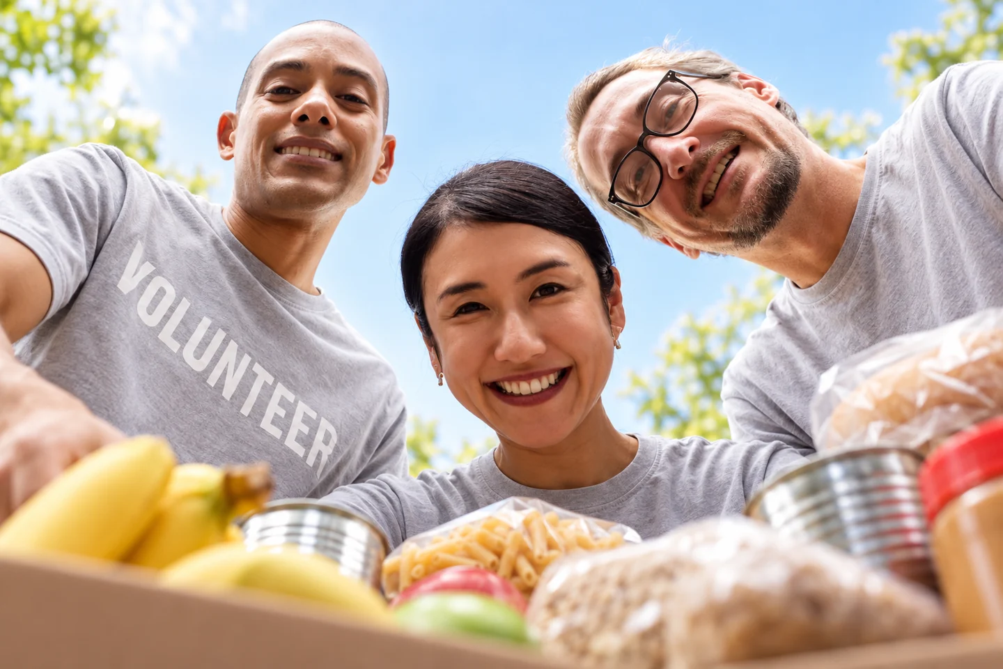 Three smiling volunteers gathered around a box of donated groceries