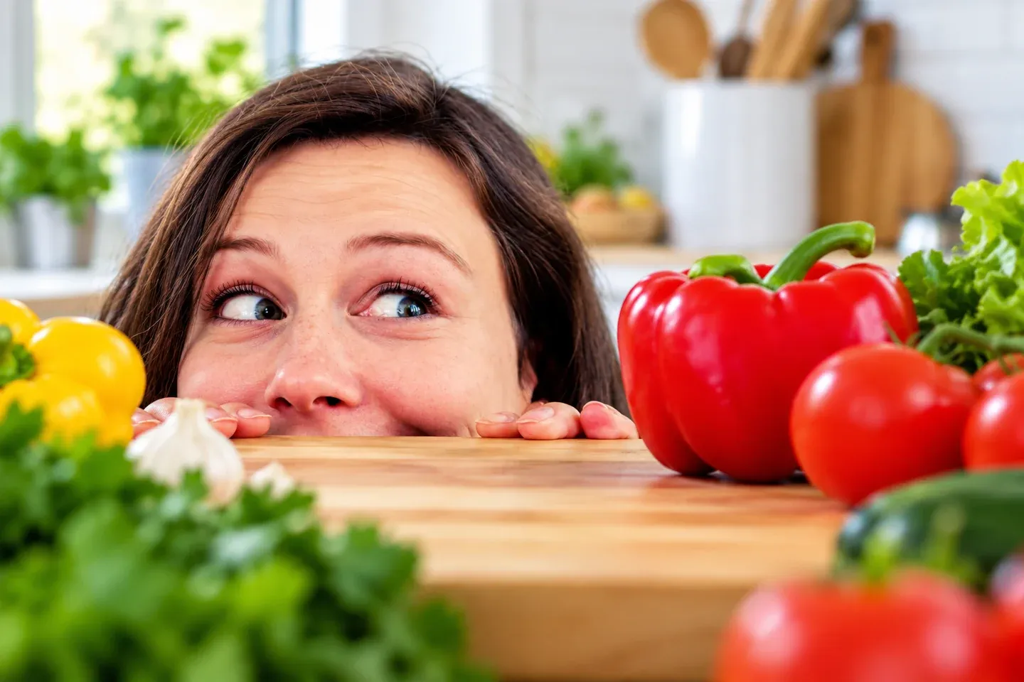 A curious woman peeking over a counter of colorful fresh vegetables